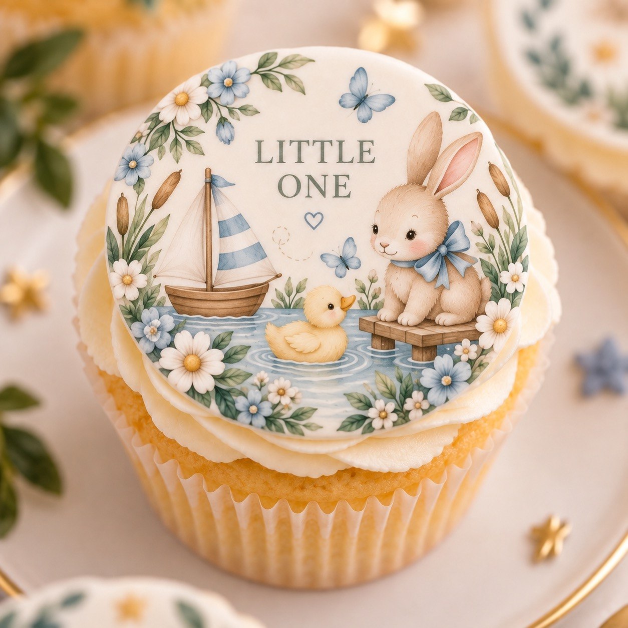 Cupcake topped with the Little One — Bunny & Boat edible fondant circle — bunny, duckling and sailboat on a pond framed by blue wildflowers